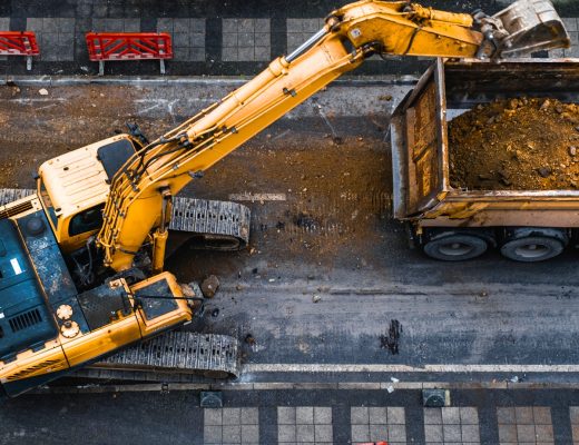 An overhead view of an excavator with a bucket attachment dumping debris into a dump truck on a construction site.