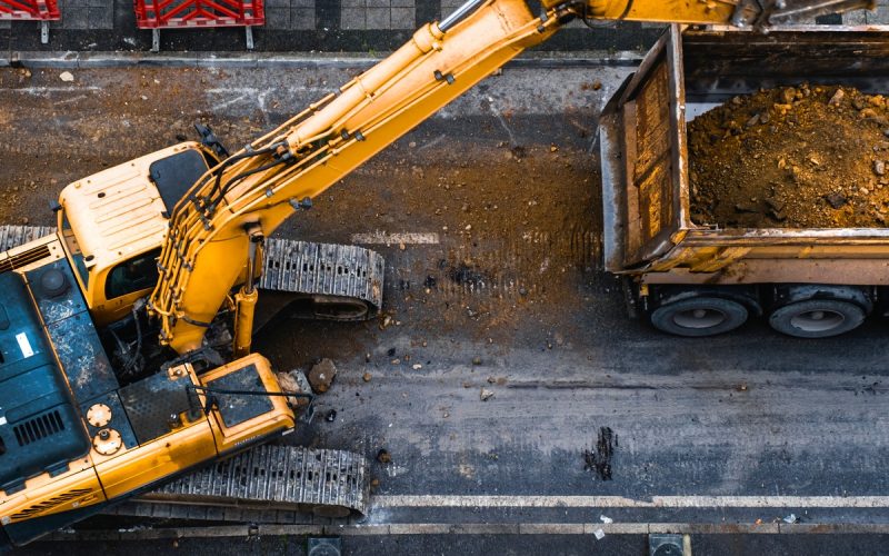 An overhead view of an excavator with a bucket attachment dumping debris into a dump truck on a construction site.