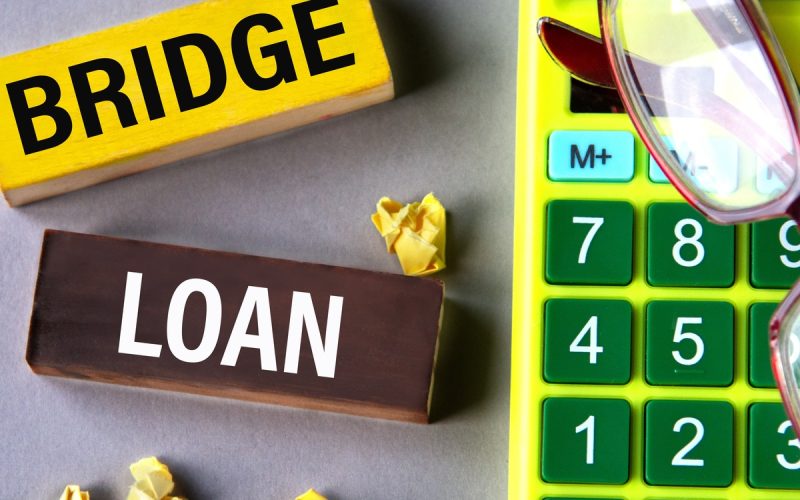 a yellow "Bridge" block and a brown "Loan" block lying beside crumpled paper, a green calculator, and eyeglasses.