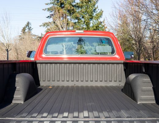 The back of a red turbo diesel truck with the trunk bed open. The truck bed is empty and clean with trees in the background.