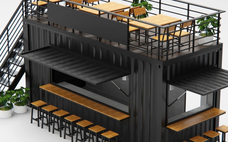 Black shipping container café with rooftop patio, outdoor bar seating, metal staircase, and modern tables with plants.