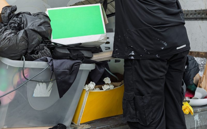  Person loads mixed household waste, cardboard boxes, and storage bins into a truck for bulk junk removal.