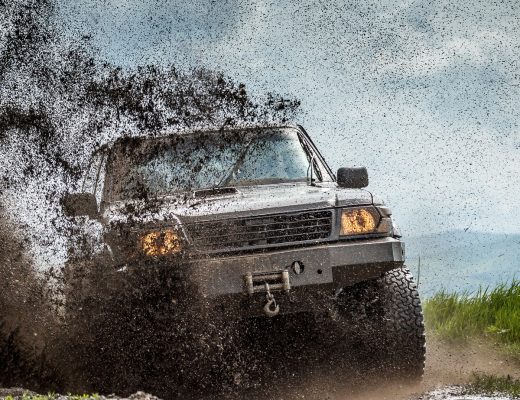 A large truck driving fast on an off-road trail during the daytime. Soil flies off the terrain as the truck drives.