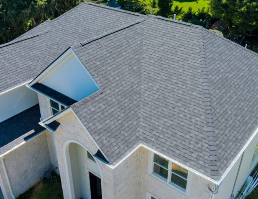 A large house with gray asphalt shingle roofs, stone siding, white trim, and a large yard near the property.