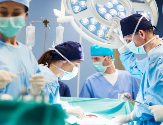 A surgical team wearing masks, scrubs, and gloves while performing an operation under bright surgical lights.