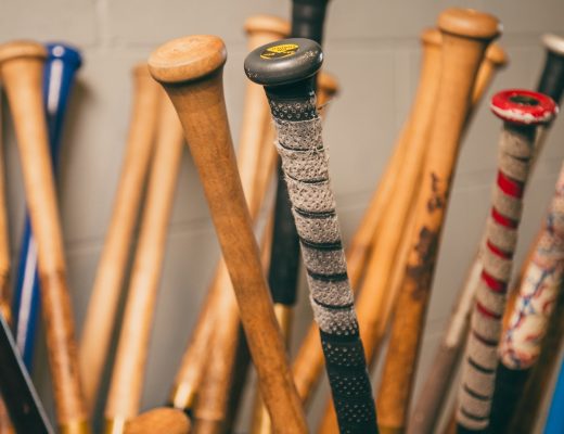 A close-up of a bin holding numerous baseball bats of various colors with the bats upside down showing their handles.