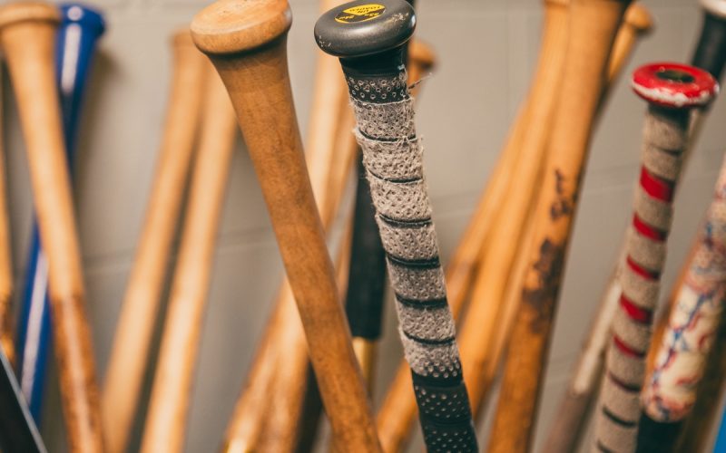A close-up of a bin holding numerous baseball bats of various colors with the bats upside down showing their handles.
