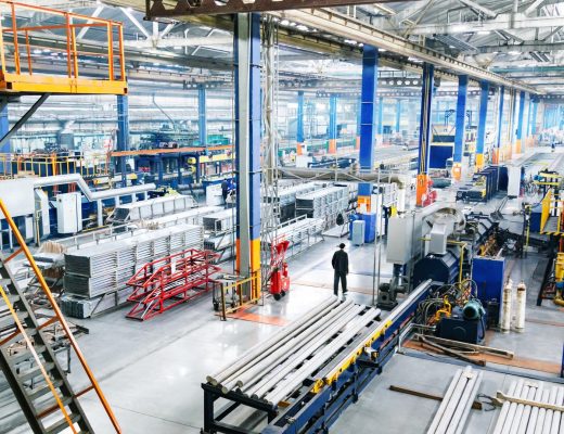 A factory with multiple heavy pieces of machinery. There is a person dressed in black that is walking through the facility.