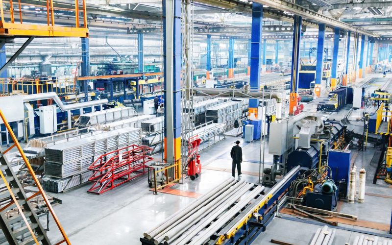 A factory with multiple heavy pieces of machinery. There is a person dressed in black that is walking through the facility.