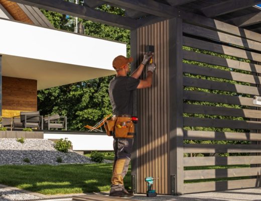 A close-up of a person using a power tool to build an outdoor structure with framing lumber and support posts.