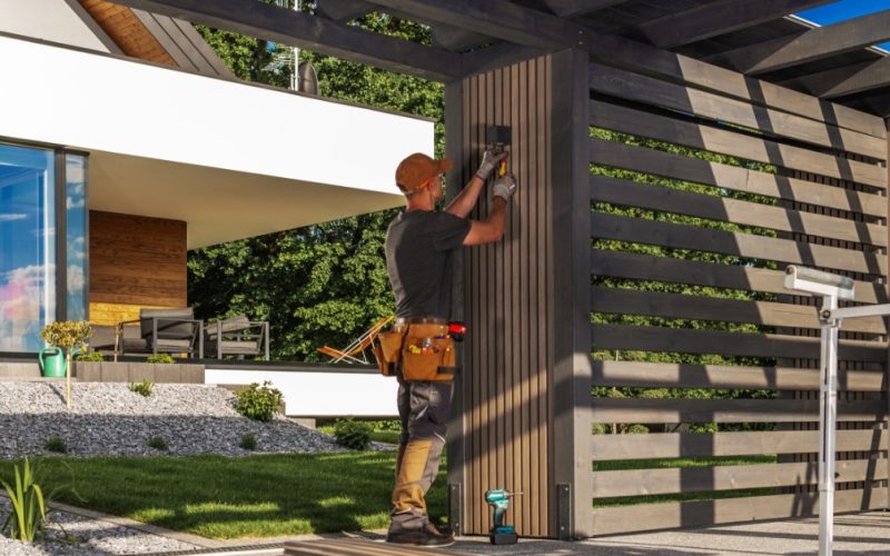 A close-up of a person using a power tool to build an outdoor structure with framing lumber and support posts.