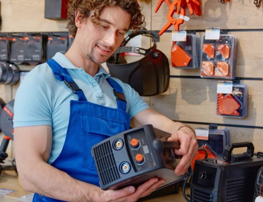 A close-up of a person in work overalls examining a welding machine on a shelf inside a hardware store aisle.