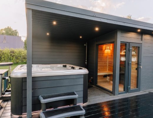 The backyard of a home with a raised deck that includes a hot tub covered by an adjoining cabin and sauna.