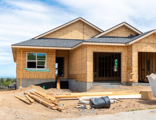 A view from the street of a one-story home with an attached, two-stall garage on a hilltop under construction.