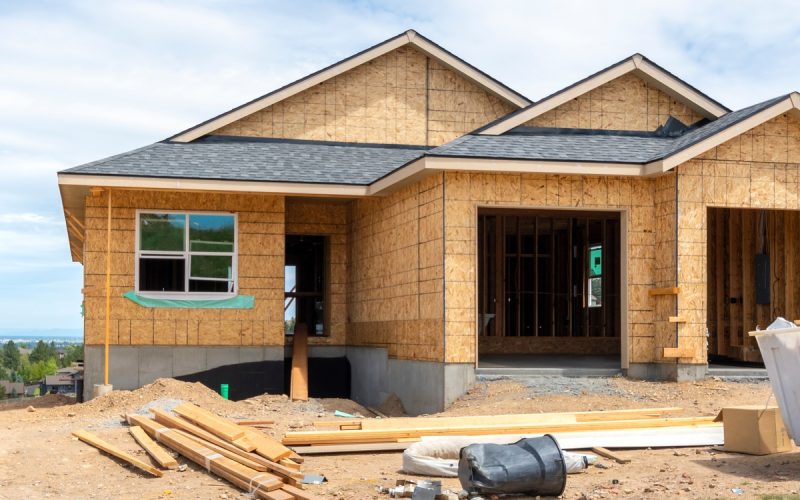 A view from the street of a one-story home with an attached, two-stall garage on a hilltop under construction.
